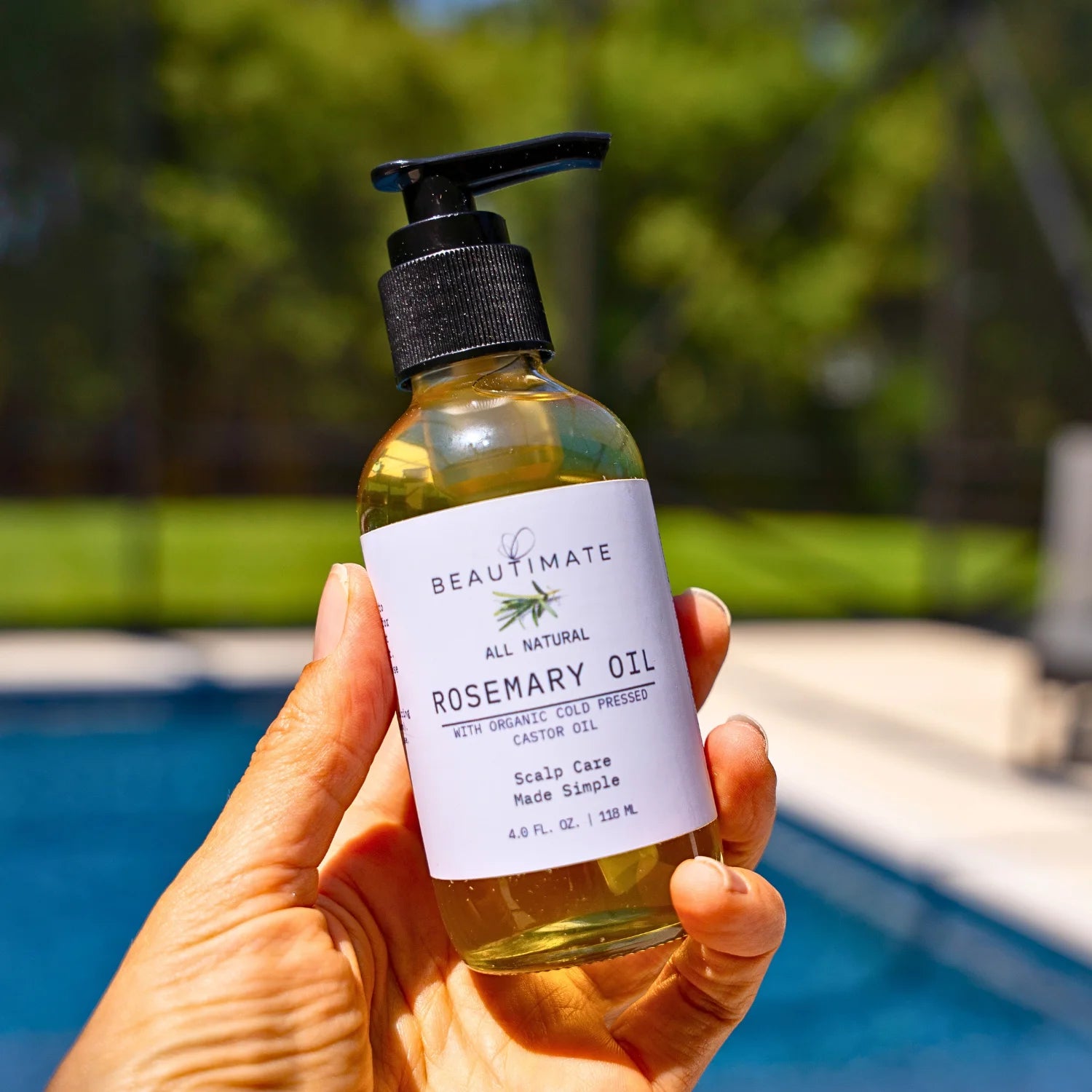 hand holding organic castor oil with rosemary with pool in the background