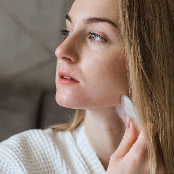 Rose quartz gua sha tool used with serum or face oil as part of a relaxing facial massage routine.