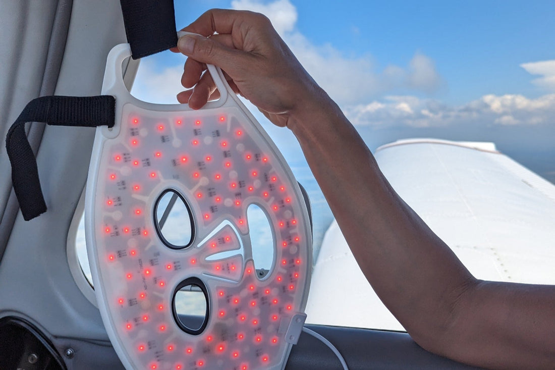 Person holding a device with red LED lights inside a vehicle, looking out the window at a blue sky.