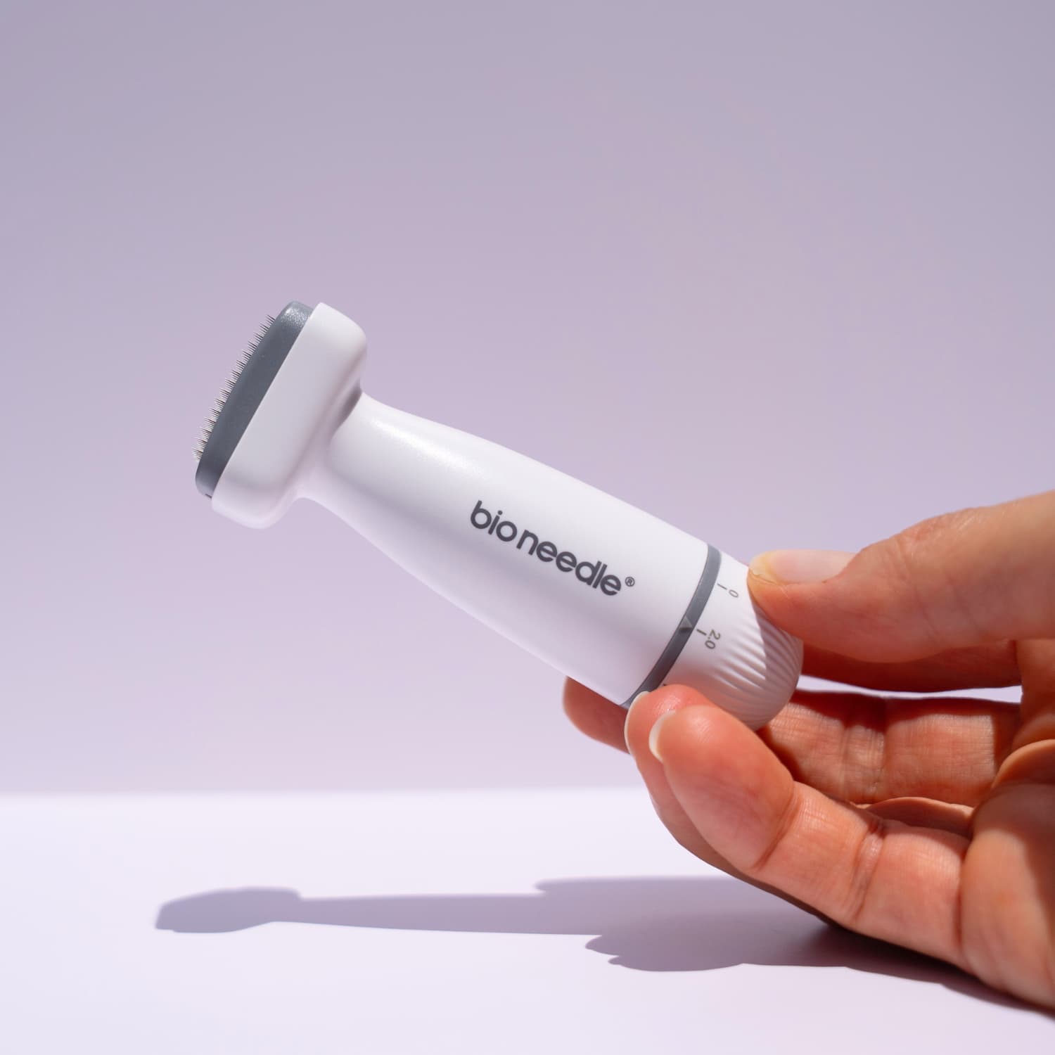 Hand holding a white and gray 'beautimate derma stamp' device against a light purple background