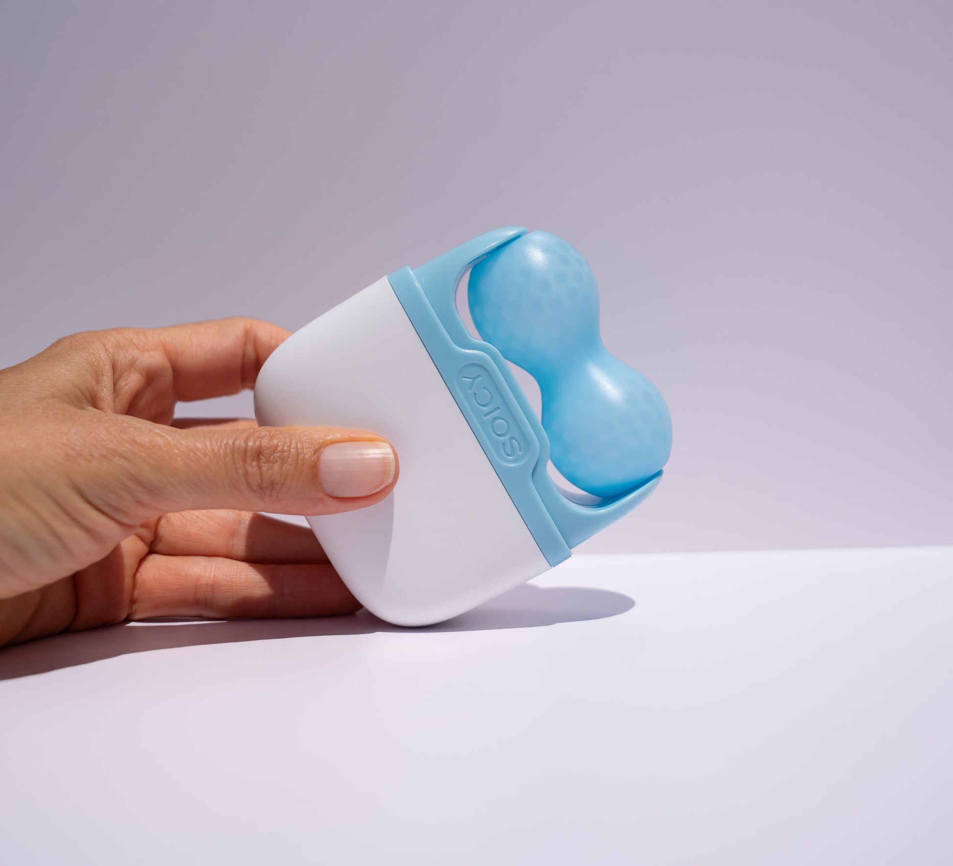 Hand holding a blue ice roller  on a light gray background