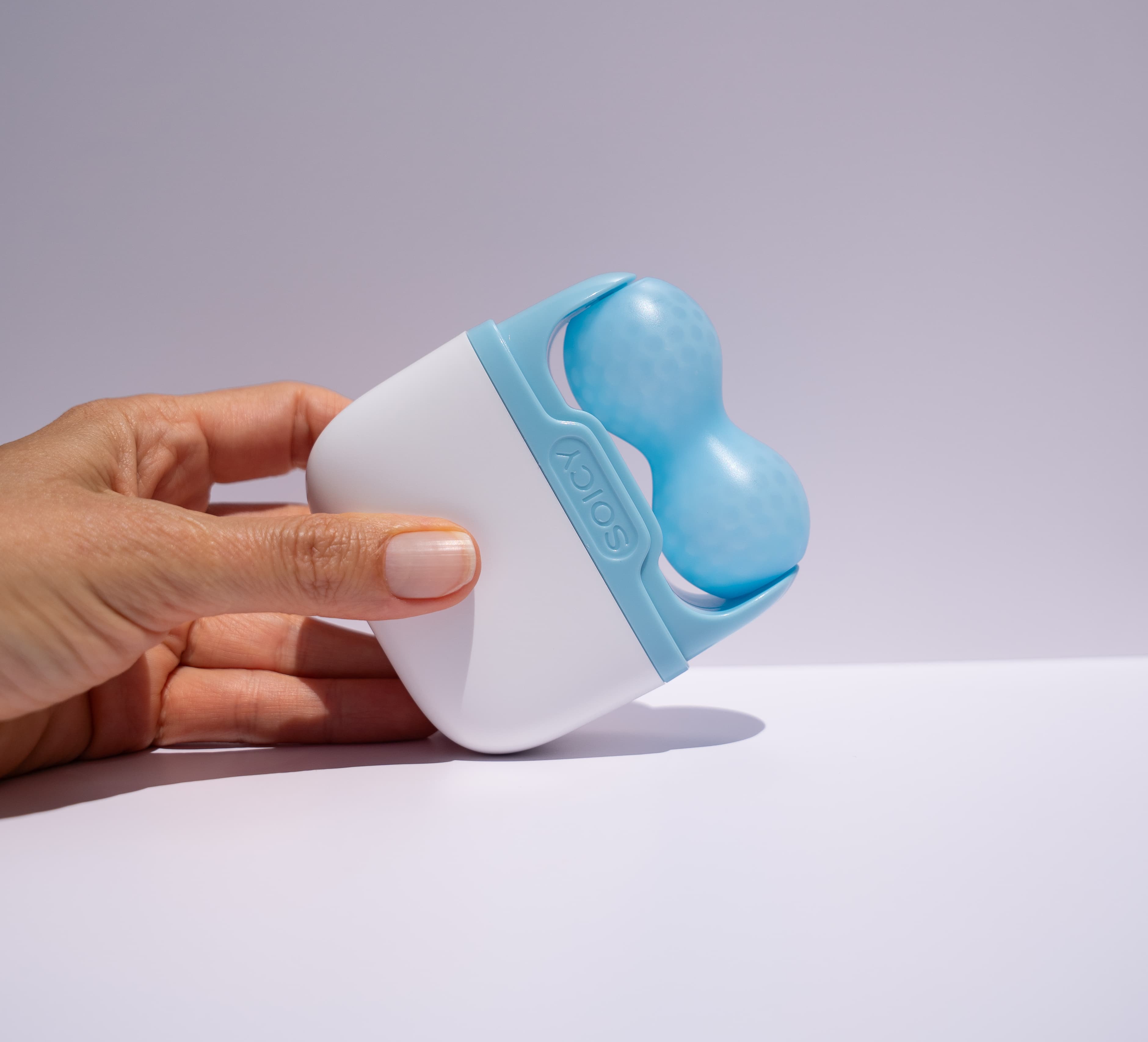 Hand holding a blue ice roller  on a light gray background