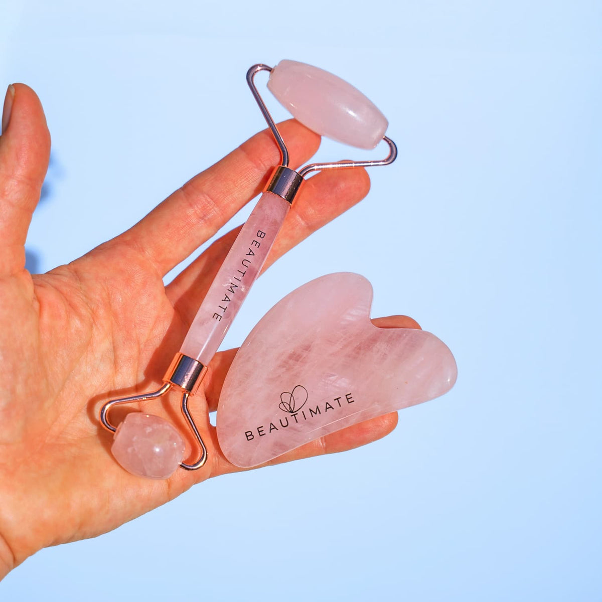 Hand holding a set of BEAUTIMATE skincare tools against a light blue background
