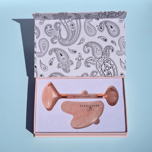 Rose gold facial roller with paisley patterned box on a light blue background