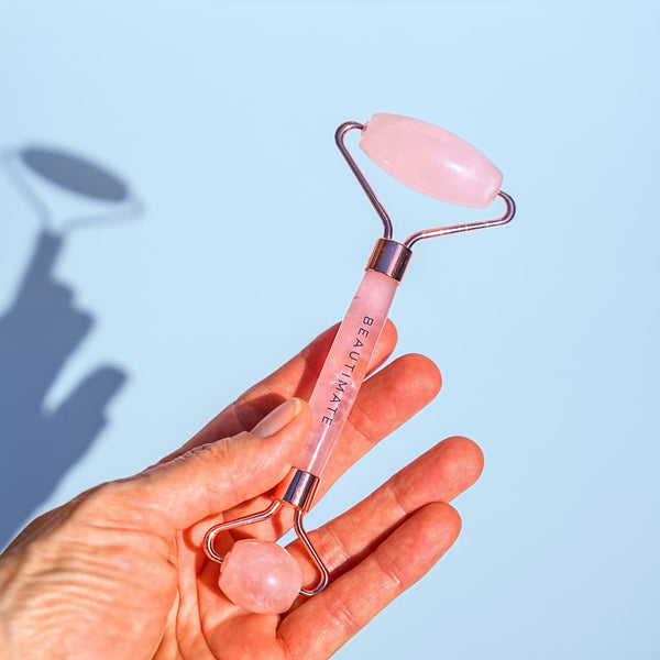 Hand holding beautimate jade beauty roller against a light blue background